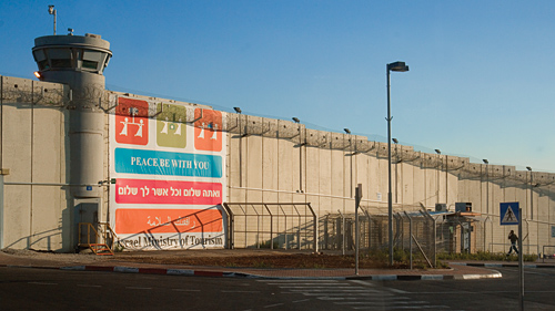 The separation barrier between Israel and the West Bank, as seen from a checkpoint on the Israeli side, with a banner on it that reads 'Peace be with you' in English, Hebrew and Arabic.
