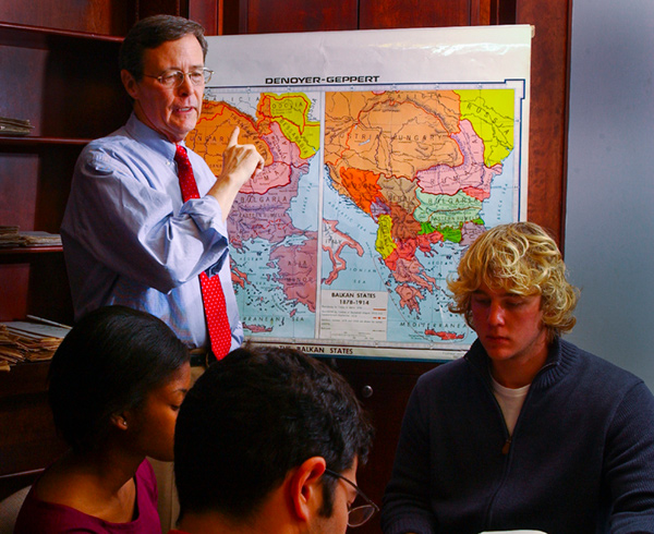 Black teaching a class in 2004, lecturing to students in a seminar room in front of a map