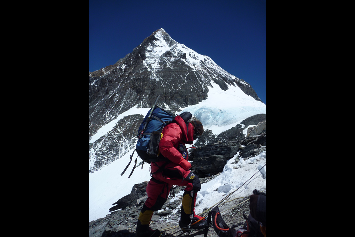 Colin Merrin wearing climbing equipment and moving upwards with peak in background