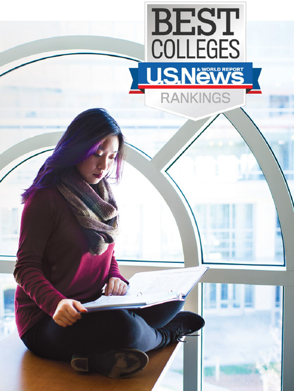 A woman studies a notebook while sitting crosslegged in front of a arched window with Emory buildings in the background. US News and World Report logo superimposed.