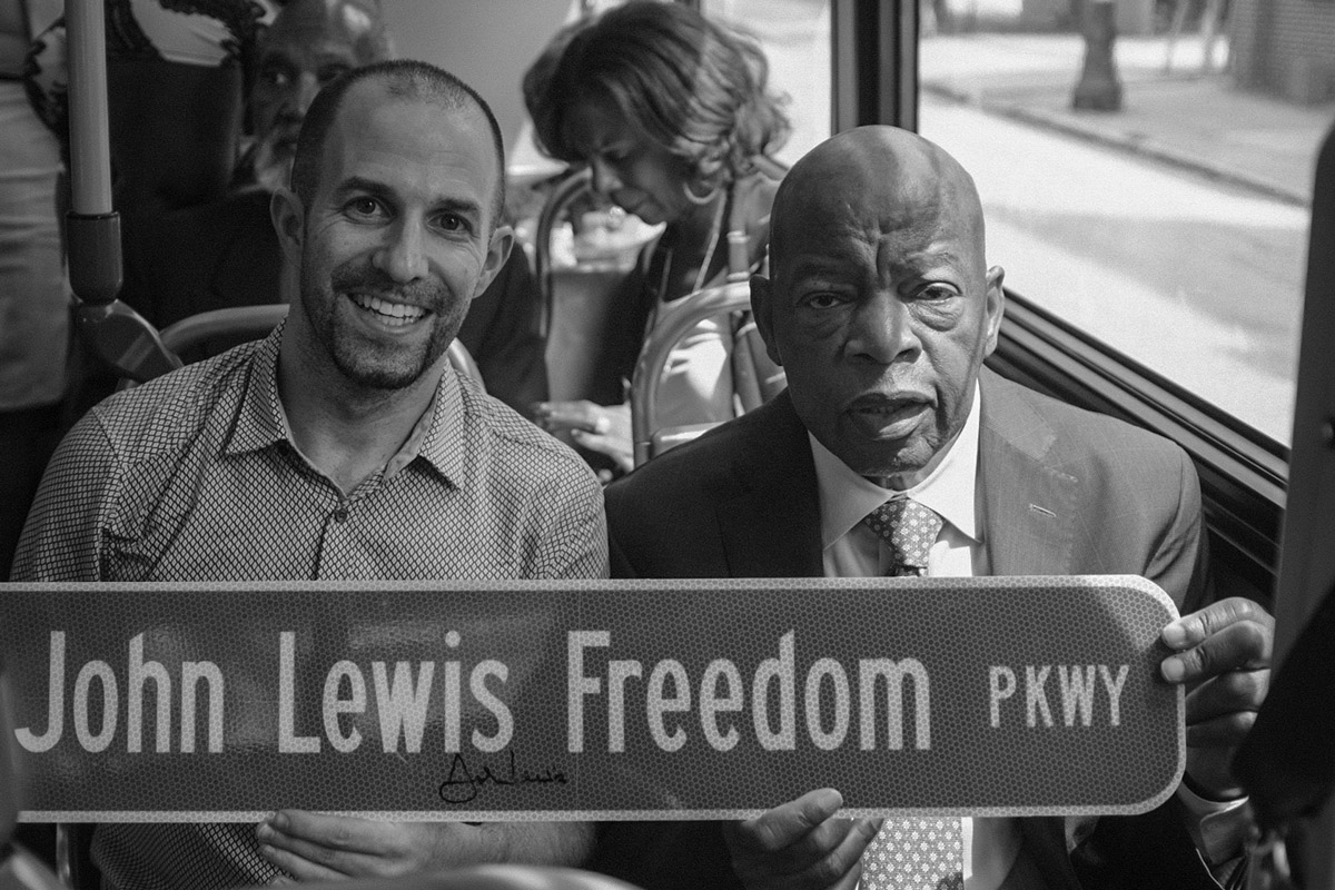 Emory alumnus Ben Arnon poses on a bus with the late Congressman John Lewis, the two of them holding a street sign that reads John Lewis Freedom Parkway