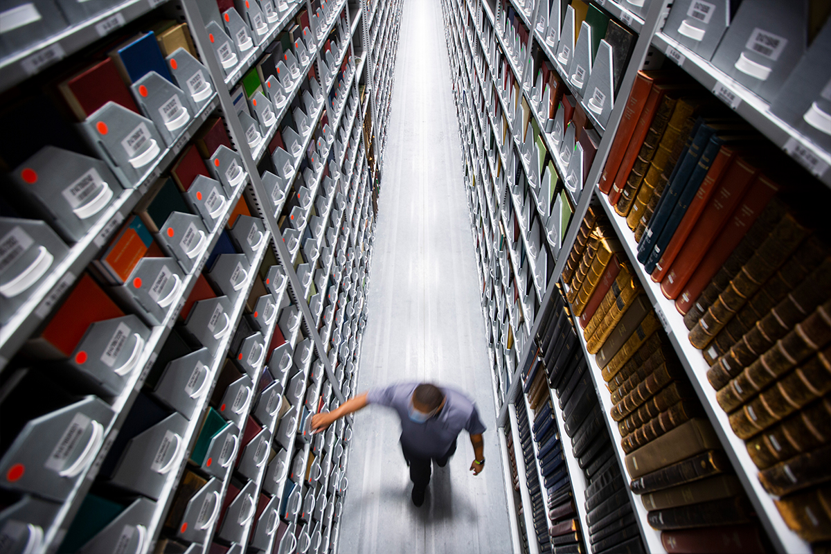 View from above of a person walking between bookshelves in the library stacks