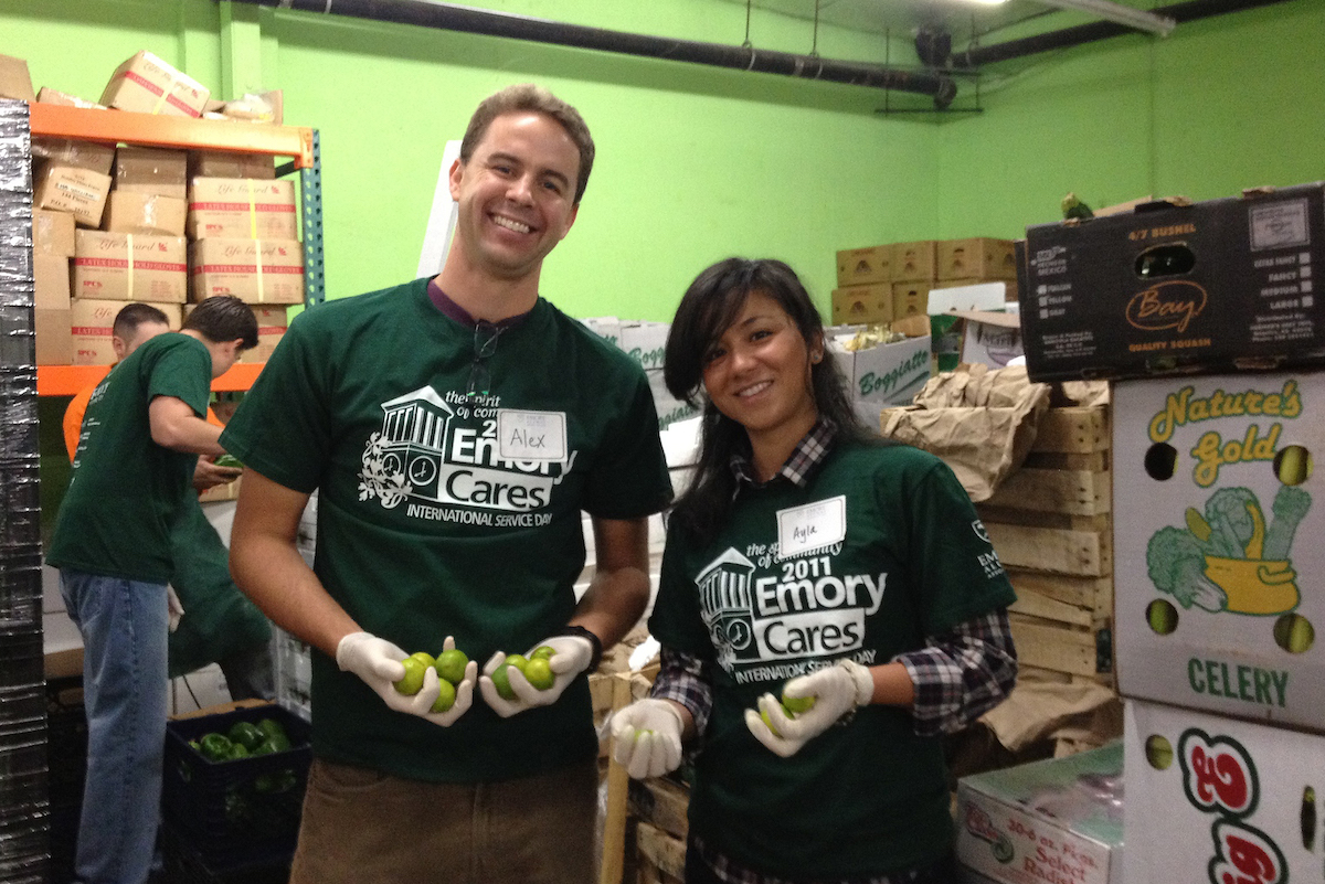 Photo of volunteers holding vegetables with other wokers and boxes of produce in background.